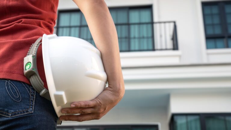 A builder staring up at their house while holding their hard hat.